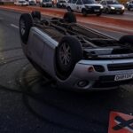 Carro capotado em rodovia no DF após acidente com motorista embriagado, viatura policial ao fundo.