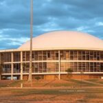 Fachada da CLDF em Brasília com bandeira arco-íris desbotada no chão, representando falhas na proteção à população LGBTQIAPN+.