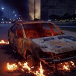 Carro em chamas com corpo carbonizado encontrado em rua do Distrito Federal, cena de investigação sem pessoas.