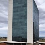 Prédios residenciais luxuosos em Brasília com Congresso Nacional ao fundo, representando privilégio controverso de servidores do DF para compra de imóveis.