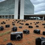 Fachada da Câmara Legislativa em Brasília com câmeras fotográficas e elementos de crise urbana, representando concurso de fotografia desnecessário.