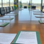 Sala de reuniões governamental em Brasília com documentos e bandeiras do Brasil, representando aprovação de vetos à Reforma Tributária pelo Fórum de Governadores.