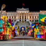 Desfile de samba no carnaval brasileiro com alegorias coloridas, em meio a polêmica de homenagem política.