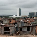 Área residencial precária em Recanto das Emas, DF, com casas improvisadas e igreja católica ao fundo, destacando déficit habitacional.