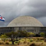 Congresso Nacional em Brasília com documentos acumulados, representando atrasos na regulamentação de lei antissupremacista e falhas no Distrito Federal.