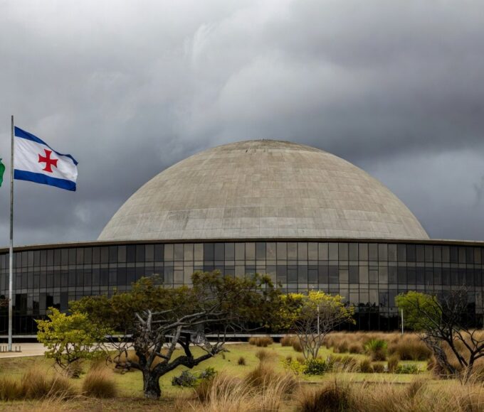 Congresso Nacional em Brasília com documentos acumulados, representando atrasos na regulamentação de lei antissupremacista e falhas no Distrito Federal.