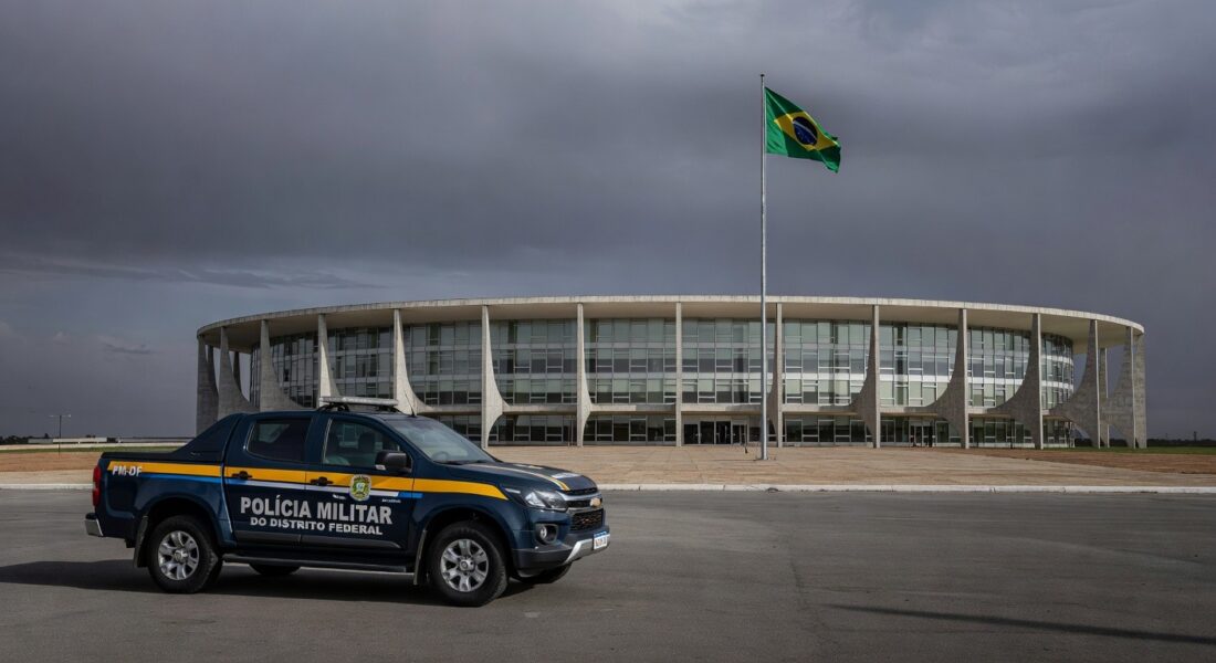 Fachada da Câmara Legislativa do DF em Brasília, com bandeiras e céu nublado, representando falhas na reintegração de policiais e impunidade contra violência à mulher.