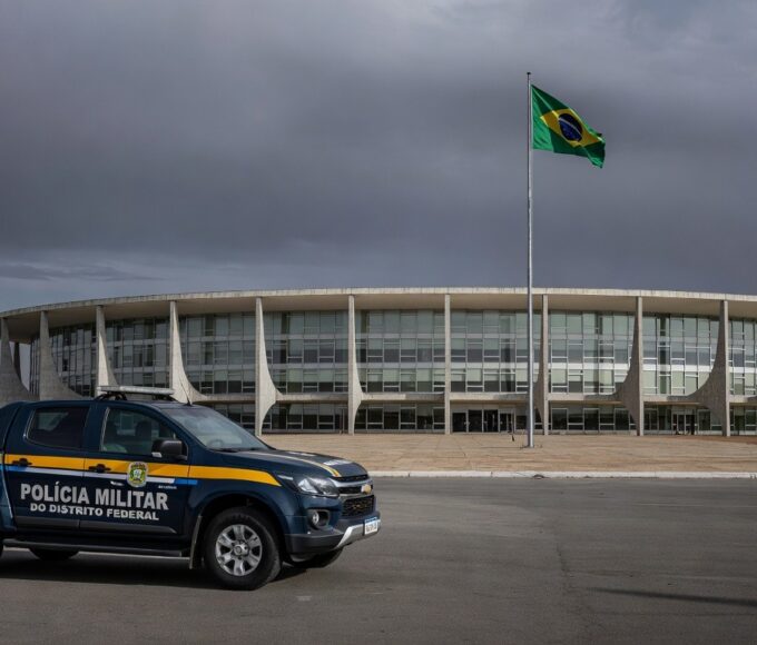 Fachada da Câmara Legislativa do DF em Brasília, com bandeiras e céu nublado, representando falhas na reintegração de policiais e impunidade contra violência à mulher.