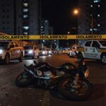 Rua vazia em Taguatinga com moto caída e fita de isolamento policial após incidente com tiros.