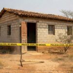 Casa simples em Águas Lindas (GO) com picareta abandonada e fita de isolamento policial, representando cena de tragédia familiar.